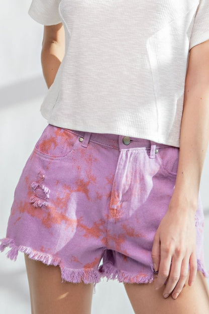 Model wearing lilac and coral tie-dye denim shorts with frayed hem, high-rise waist, and distressed detailing.